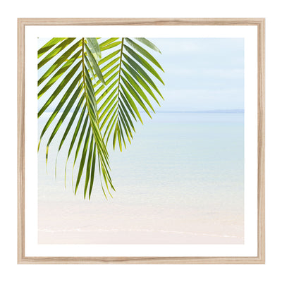 Framed artwork with green palm leaves against a tranquil beach 